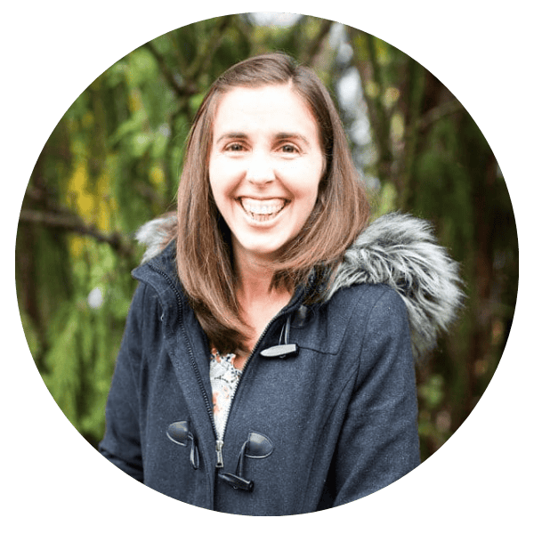 Woman with straight brown hair and fur-hooded jacket smiles amid trees